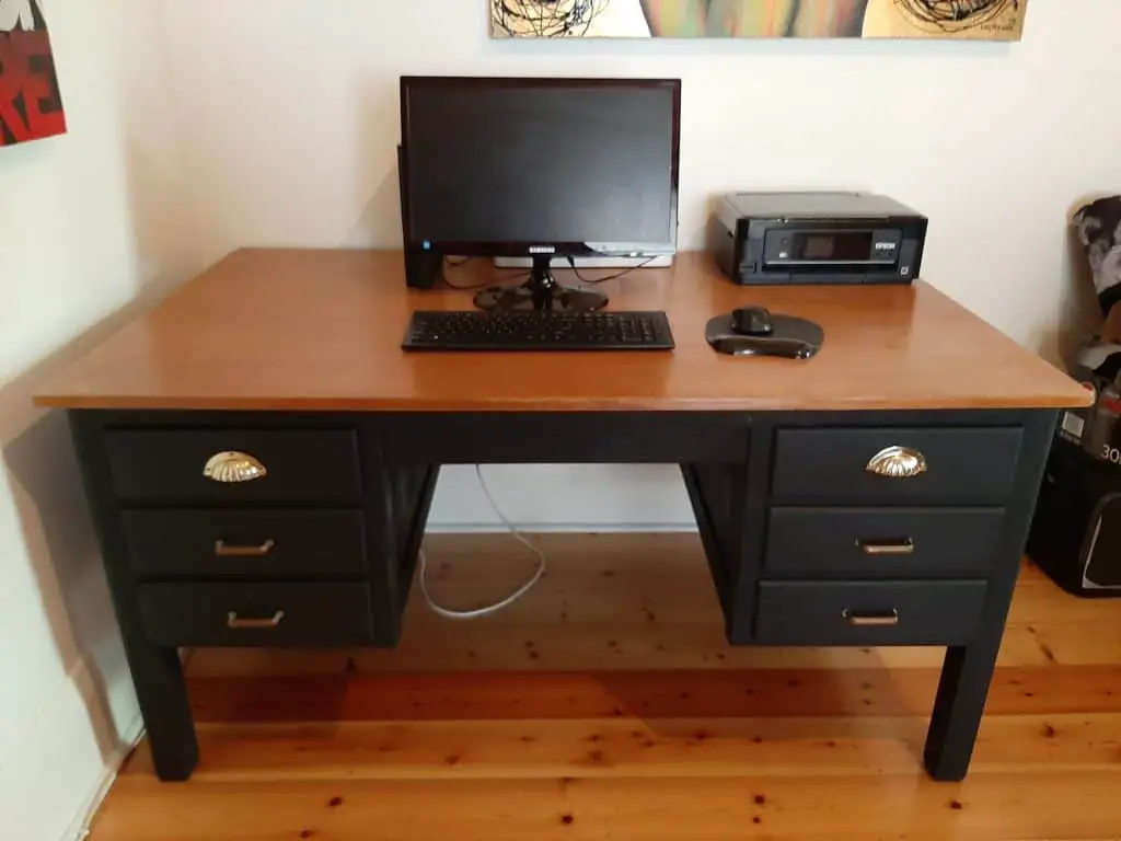 A photo of the finished desk upcycle. Wooden desk top and black matte base and legs. New gold handles.
