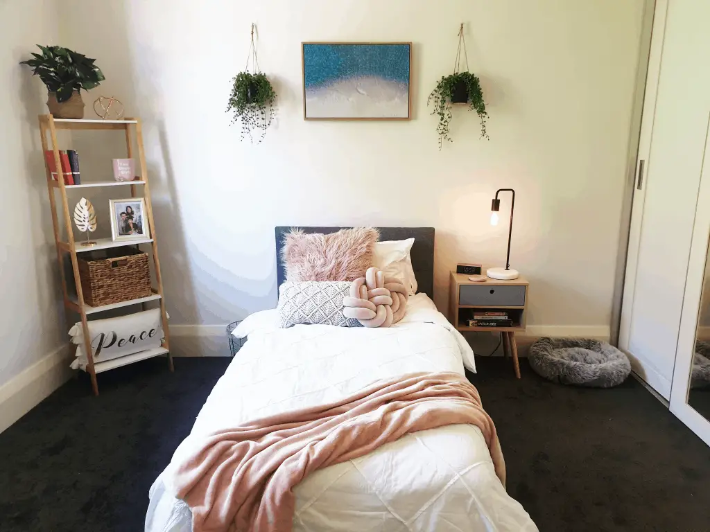 DIY Bedroom Makeover - bed with pink throw, hanging plants and picture above bed. Light bulb bedside lamp and book shelves.
