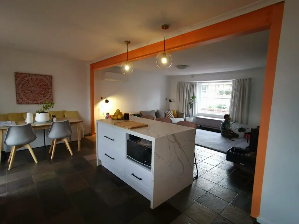 After kitchen renovation - view of living room and island bench. Microwave on island. Orange beam and columns to open up space.